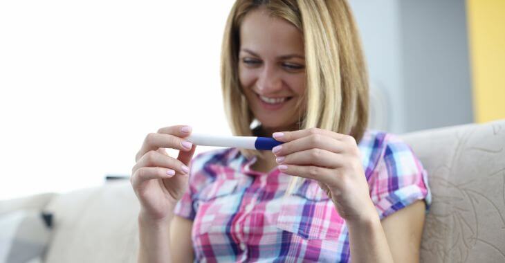 A happy woman looking at positive home pregnancy test before first pregnancy doctor visit.
