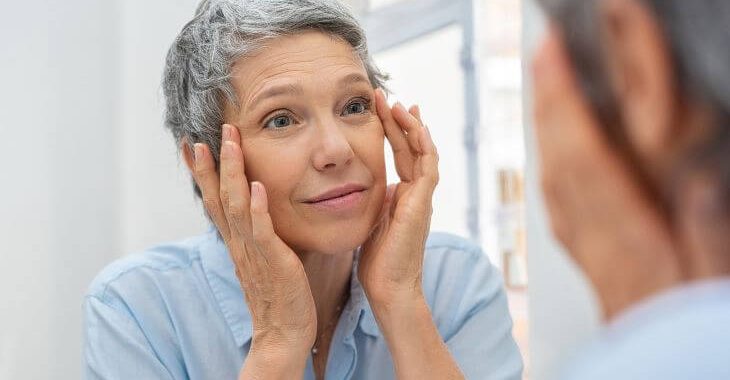 Mature woman before eye skin rejuvenation treatment looking at her face in the mirror 