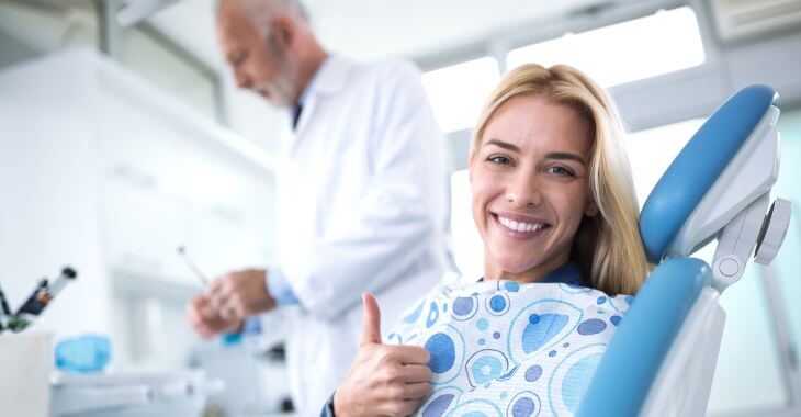 Satisfied dental patient in a dental chair during showing her thumb up