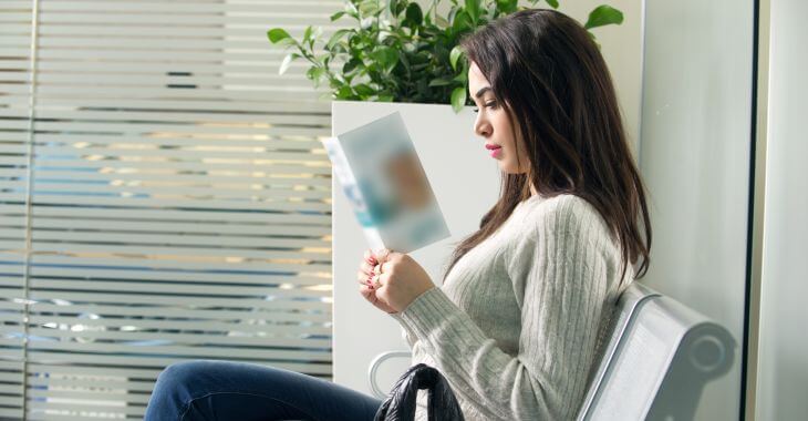 Young woman reading a brouchure while waiting for an appointment at doctor's waiting room