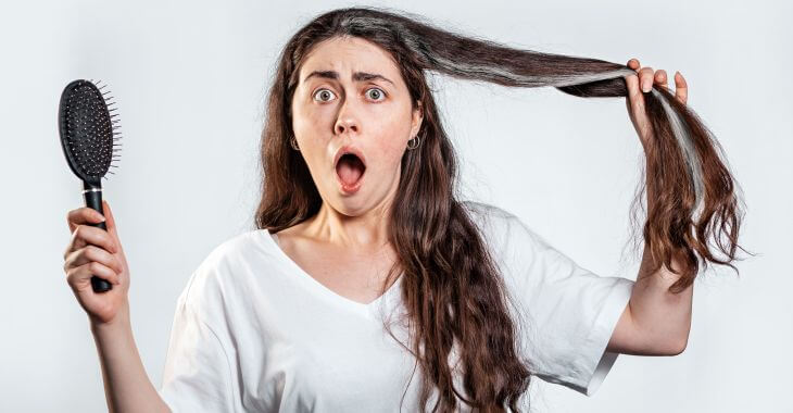 Shocked young woman suffering from Marie Antionette syndrome who has just discovered gray strand of hair.