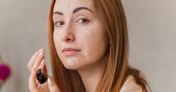 A young woman applying make up to cover acne scars.