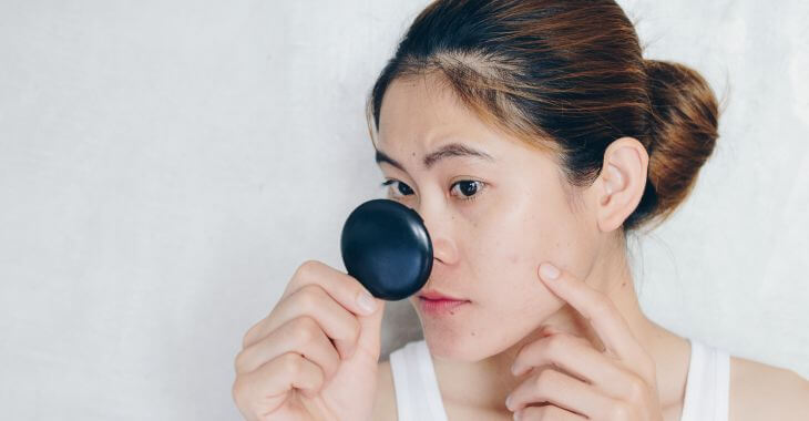 A concerned young Asian woman checking her facial skin in a mirror.