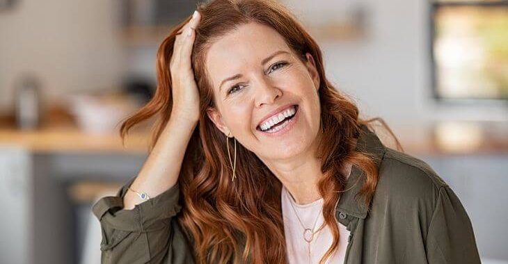 A happy middle-aged woman checking her hairline after PRP therapy for hair loss.