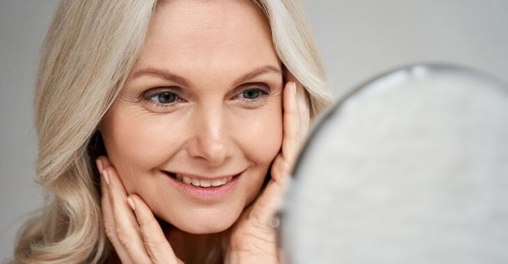 A happy woman looking at her face in the mirror.