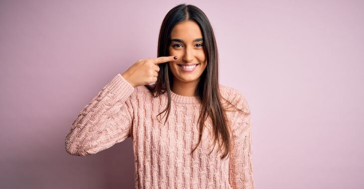 A beautiful happy woman pointing at her nicely shaped nose after non-surgical nose job procedure.