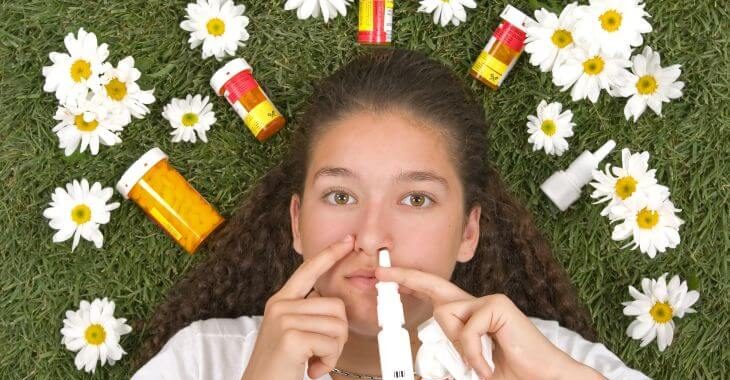 A teenage girl lying on grass among allergy medications.