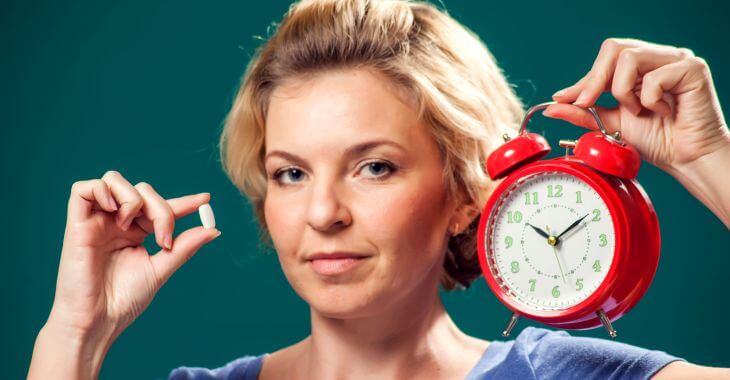 A woman holding a melatonin pill and an alarm clock.