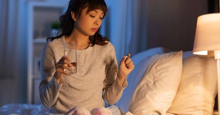 An Asian woman taking a melatonin pill before going to sleep.