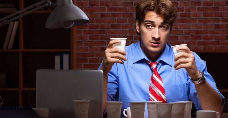 Fatigued businessman working on his laptop surrounded by empty cups of caffeine beverages.