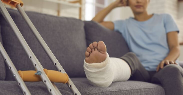 Crutches next to a woman with a broken leg in a plaster resting on a sofa.