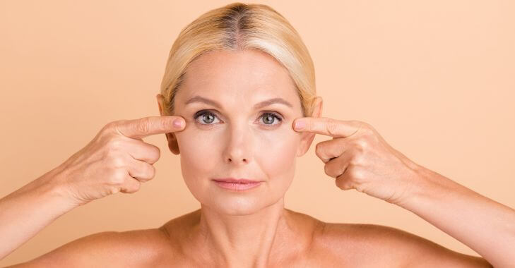 A mature woman pointing to her eyelids after non-surgical skin tightening treatment.