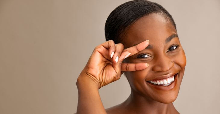 Happy Afro-American woman after eyelids cosmetic treatment pointing at her  upper and lower eyelids. 