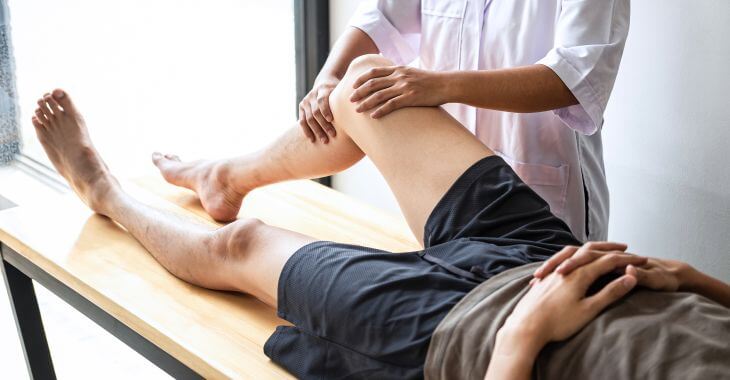 A doctor examining a lying down patient suffering from leg pain.