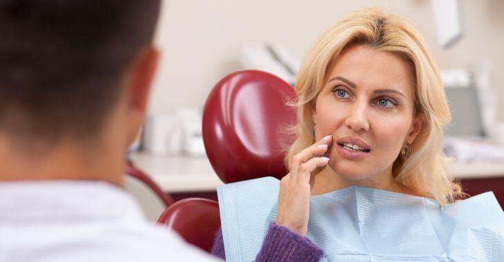 A concerned woman in a dental chair talking to a dentist.