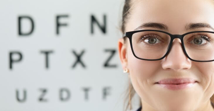 A woman wearing glasses with eye test chart in the background.