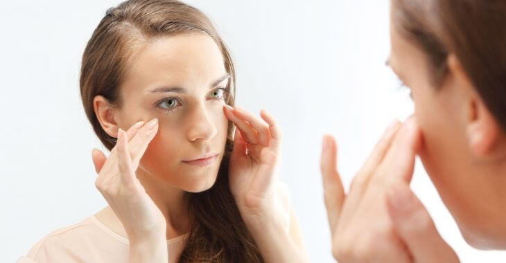 Young woman looking at her eyes in the mirror.