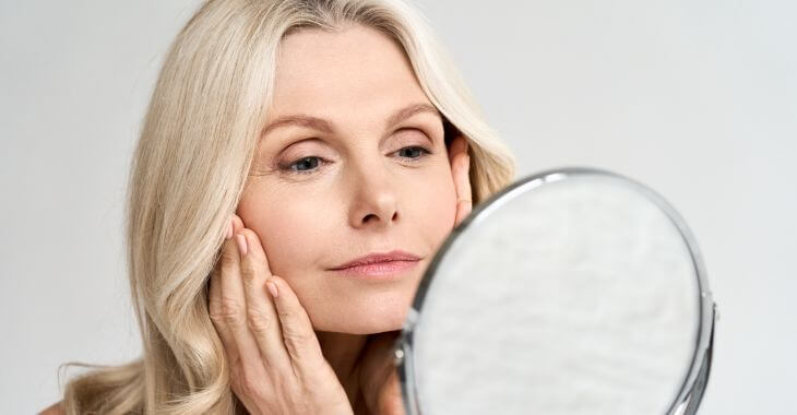 Satisfied youngish-looking mature woman looking at her face in the mirror.