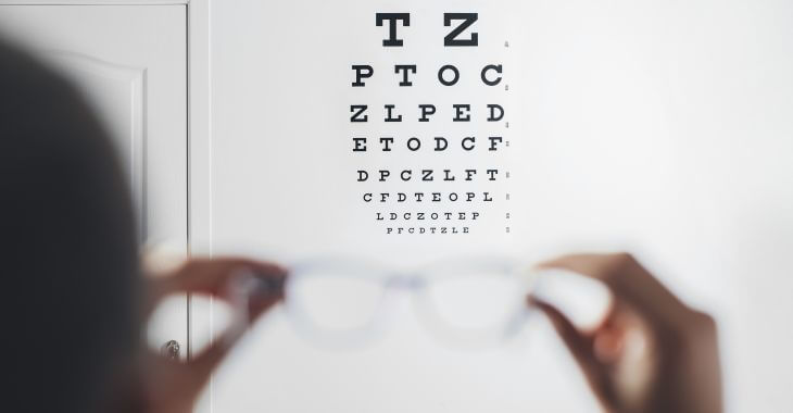 A person holding glasses in their hands trying to read letters from eye test chart.