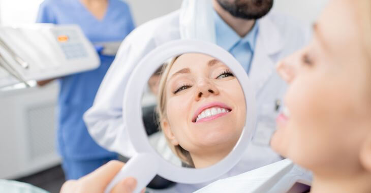 Satisfied woman in a dental chair  after tooth repair procedure  looking at her teeth in a mirror.