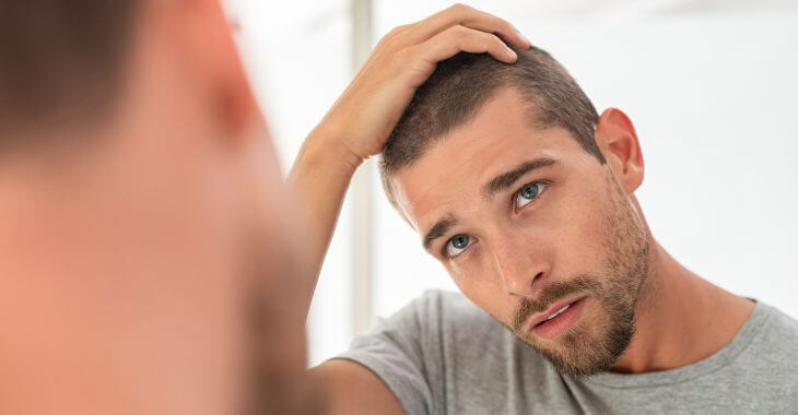 Concerned young man with short hair looking at the mirror and checking his hair length .