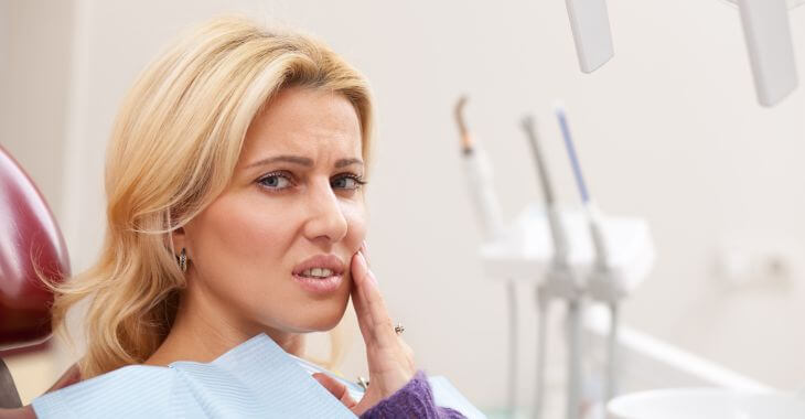 Concerned woman in a dental chair touching the mouth area.