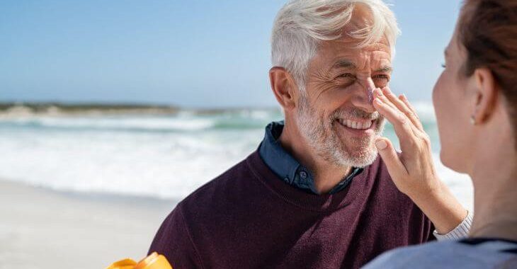 A woman applying a sunscreen on a nose of a joyful senior man spending a day on a beach.