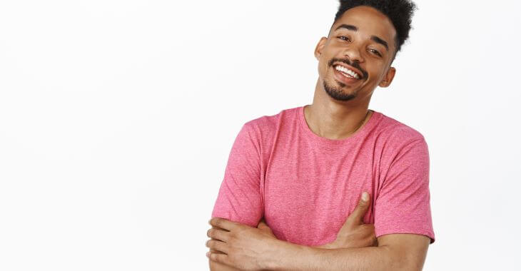 Young cheerful Afro-American man wearing a pink T-shirt with arms crossed over his breasts.