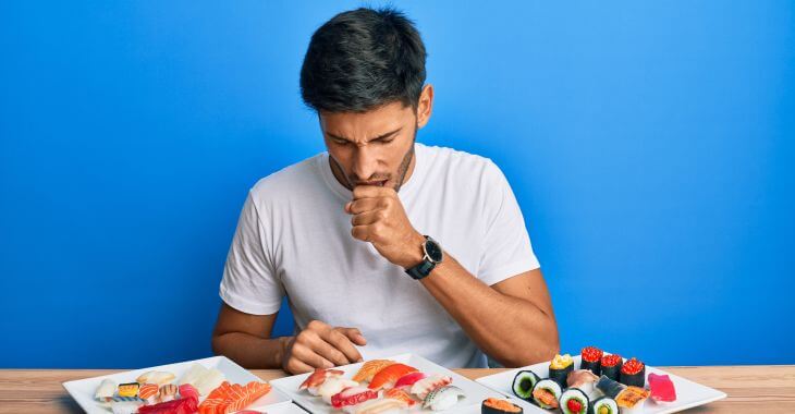 Young man at the table with food coughing after eating.