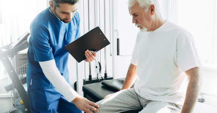 A doctor examining a knee joint of a senior man after knee replacement surgery.