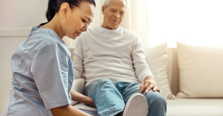 A nurse examining elder man's swollen lower leg.