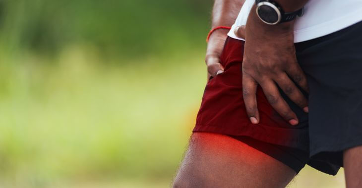 An Afro-American sportsman feeling cramp in his inner thigh.