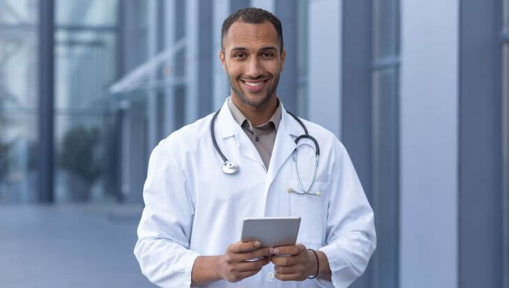 A happy man doctor with a tablet in front of a clinic. 