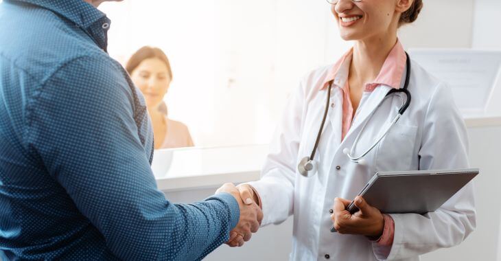 A doctor meeting and shaking hands with a patient at a reception desk.