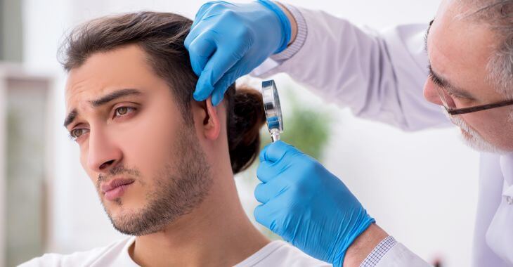 Doctor with a magnifying glass examining skin behind man's ear.