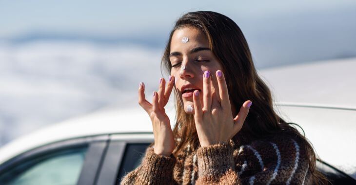 Young woman on the snow slope applying sunscreen on her face.