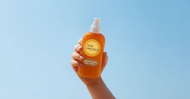 A hand holding a bottle of sunscreen lotion.
