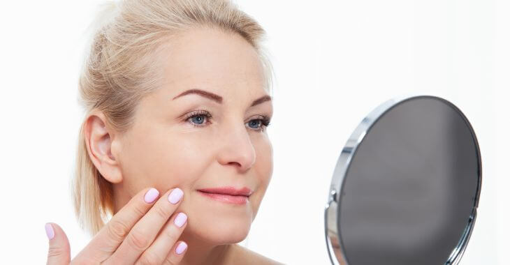 A mature woman watching her facial skin in a mirror.