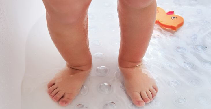 Feet of a baby standing in shower tub filled with water.