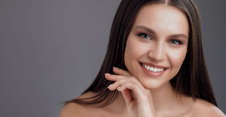 Cheerful beautiful woman after facial treatment touching face skin.