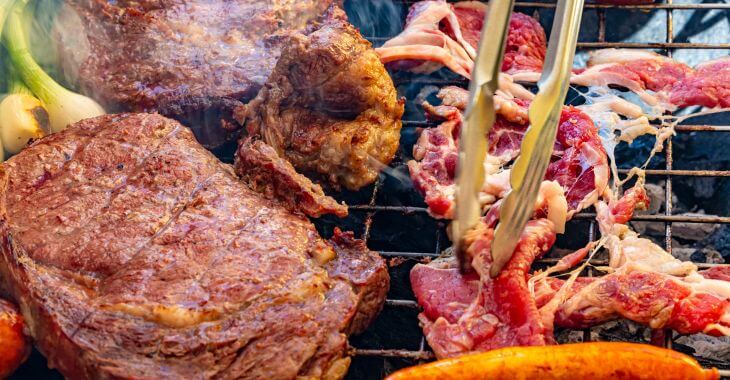 Variety of red meats being grilled.