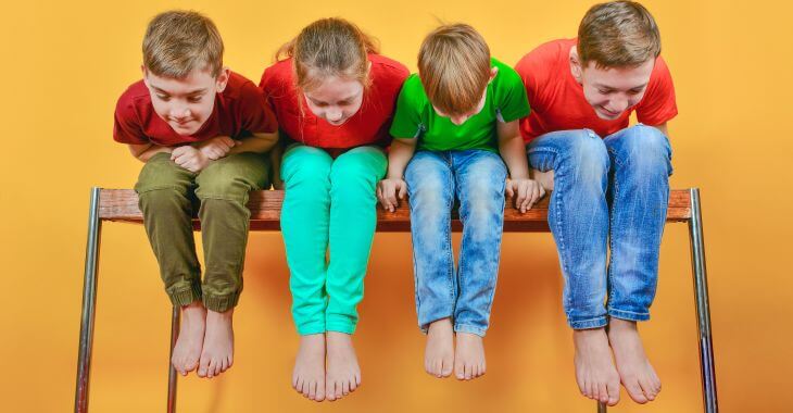 Children sitting on a high bench looking down at their legs.