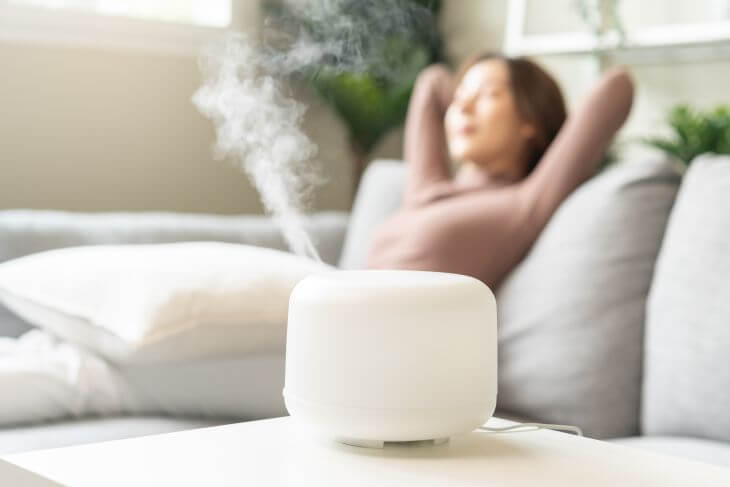 A relieved woman relaxing on a sofa next to a working humidifier.