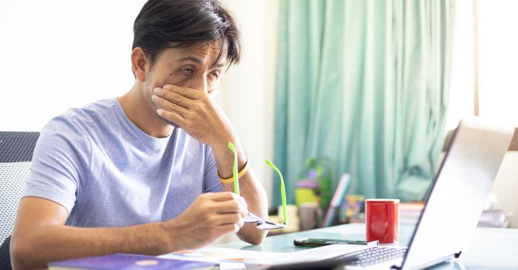 Extremely fatigued Asian man trying to work on his laptop.