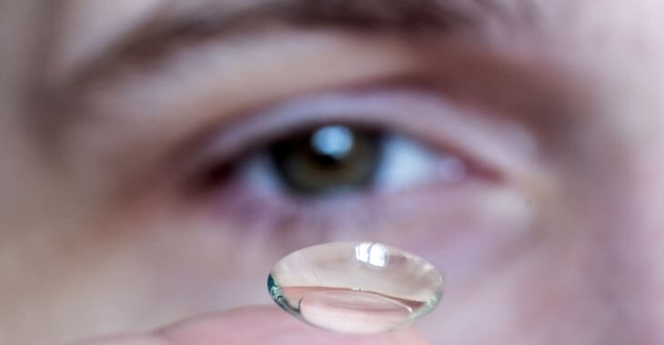A man looking at a contact lense that he is holding on the tip of his finger.