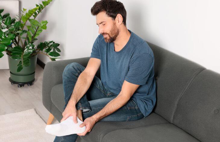 A man suffering from Baxter’s neuropathy sitting on a sofa and massaging his foot.