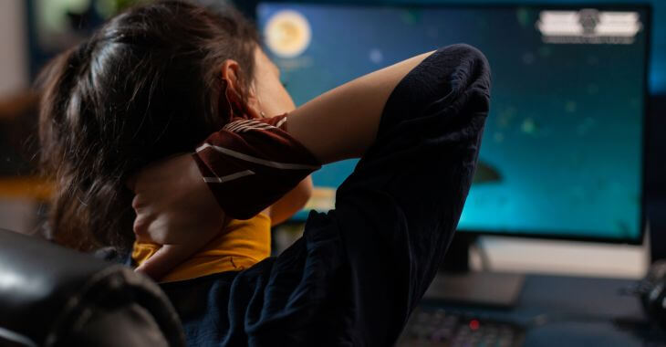 Young woman in front of a computer suffering from gamer neck pain.