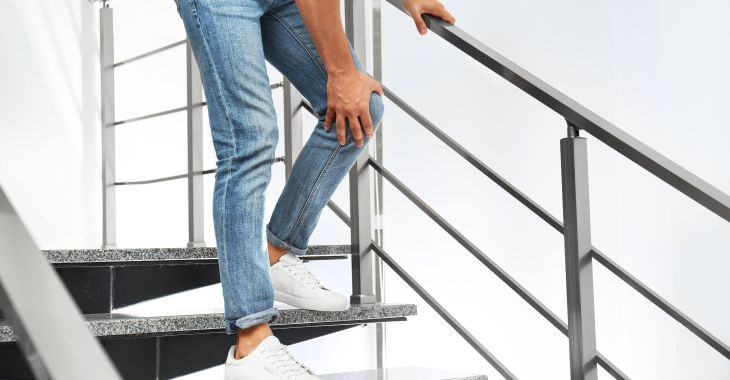 A person feeling knee pain when going down the stairs.