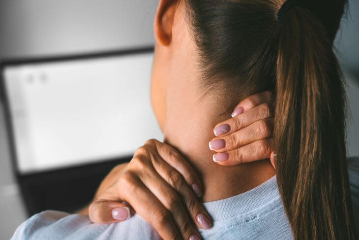 A woman working on a laptop massaging back of her neck and shoulder.