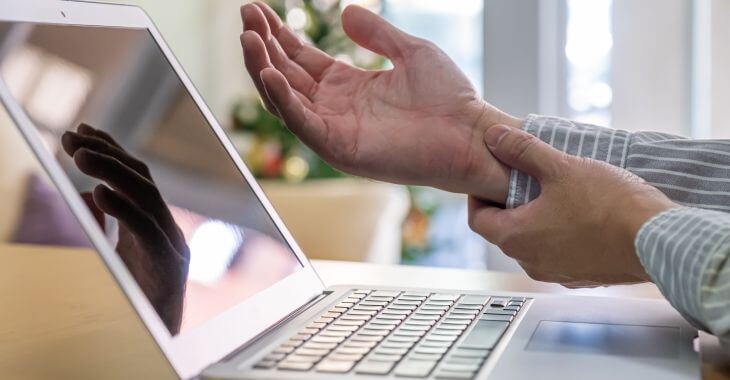 A man at the desk with laptop pressing and massaging his painful wrist.